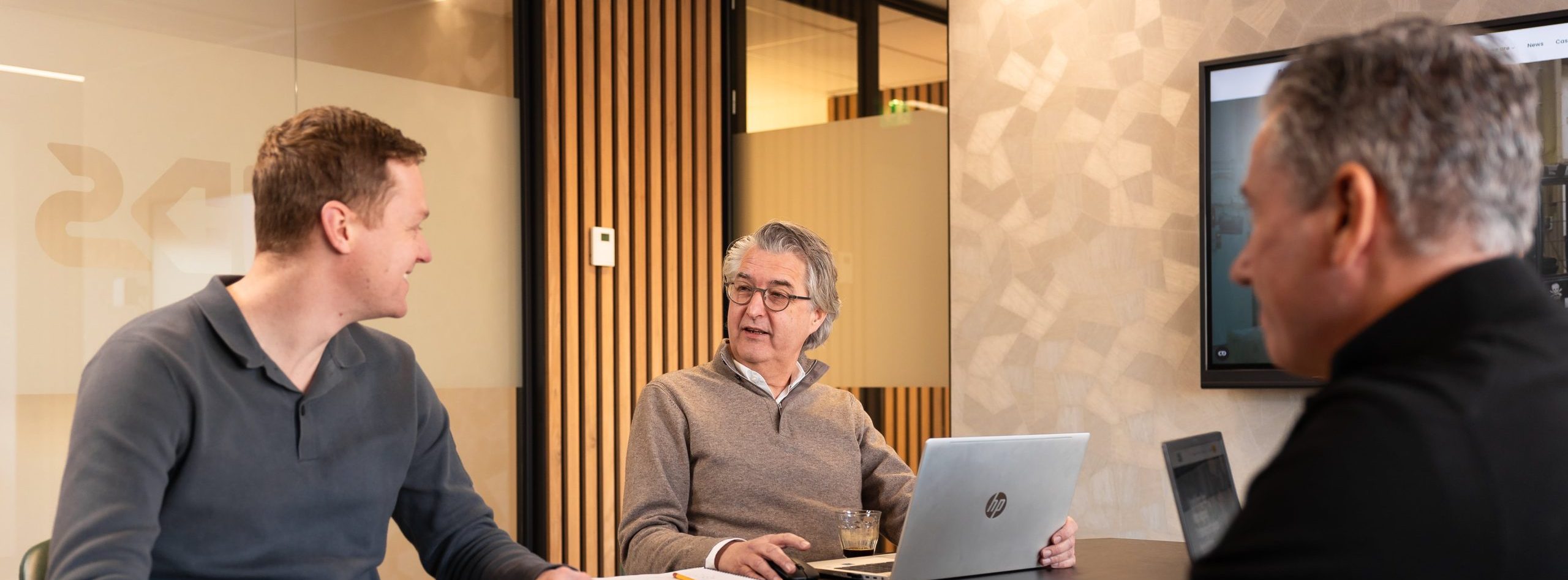 three people around a meeting table are looking at each other and discussing things