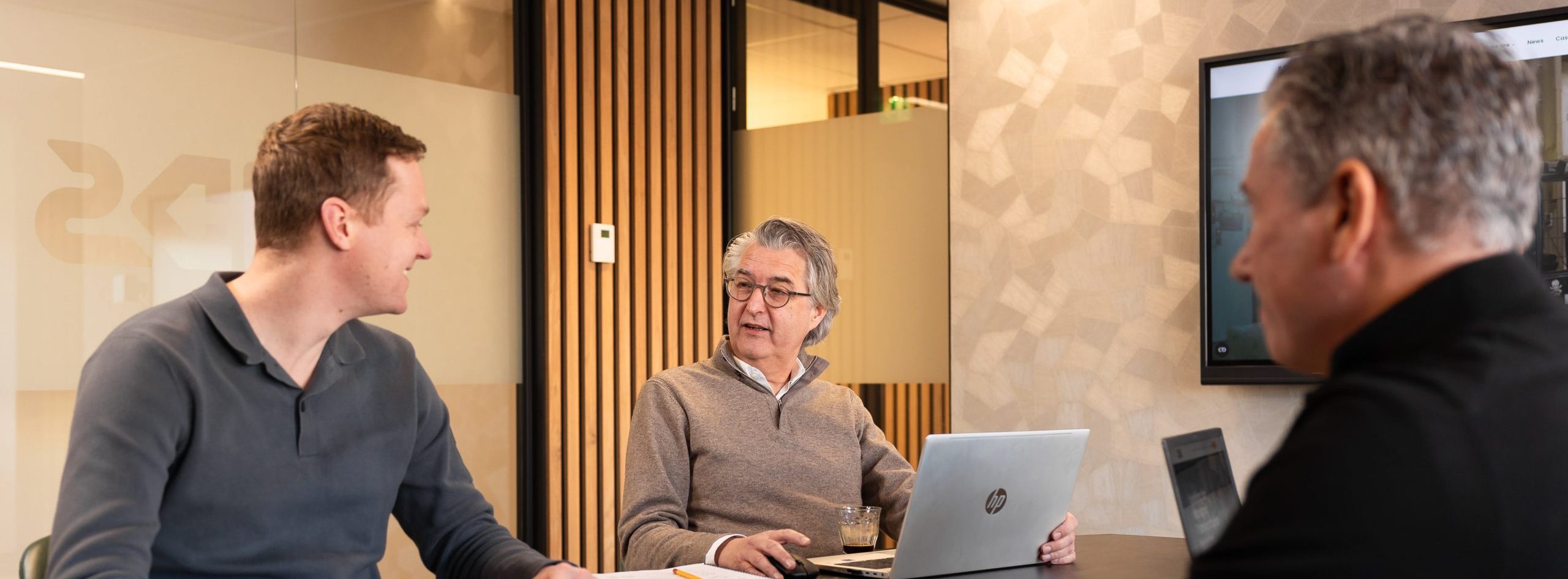 three people around a meeting table are looking at each other and discussing things