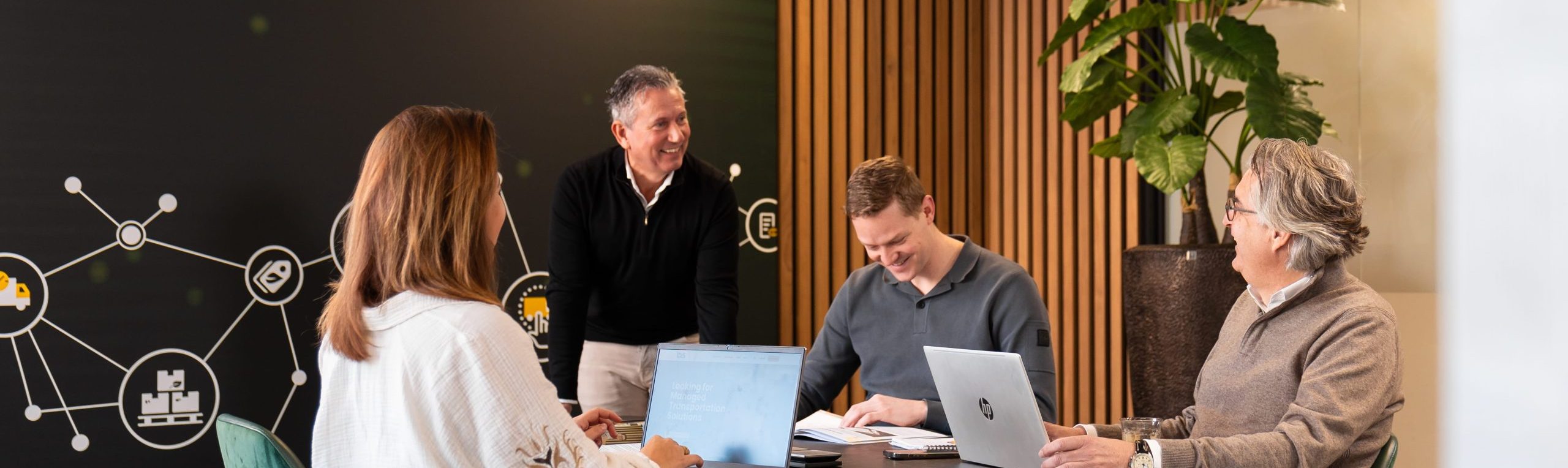 Four people are gathered around a table staring at eachother and smiling.