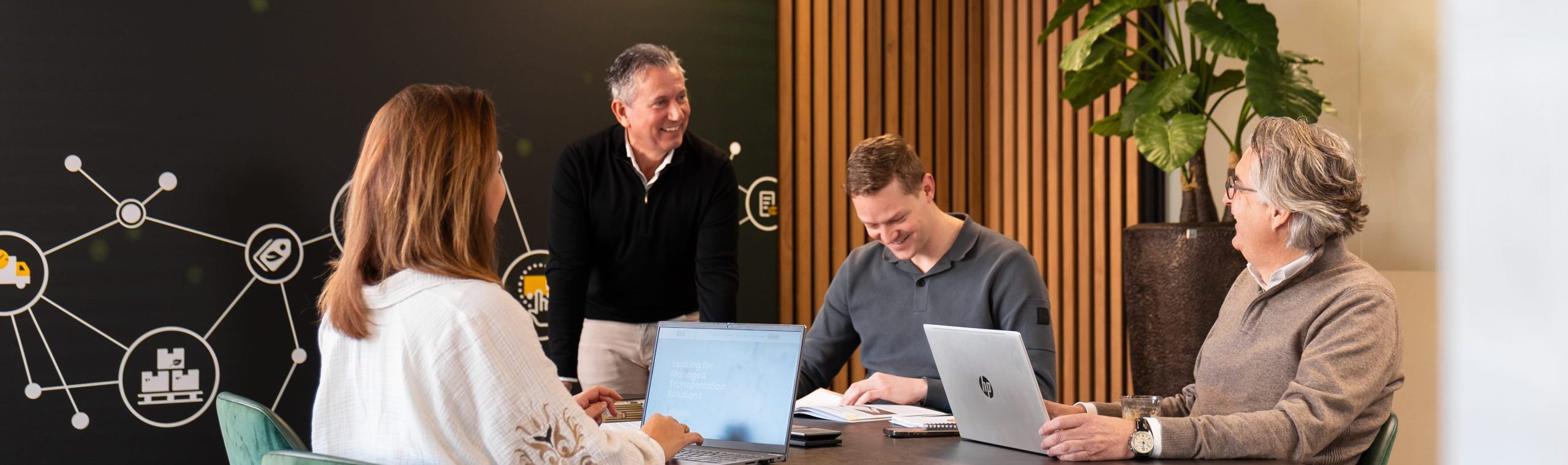 Four people are gathered around a table staring at eachother and smiling.