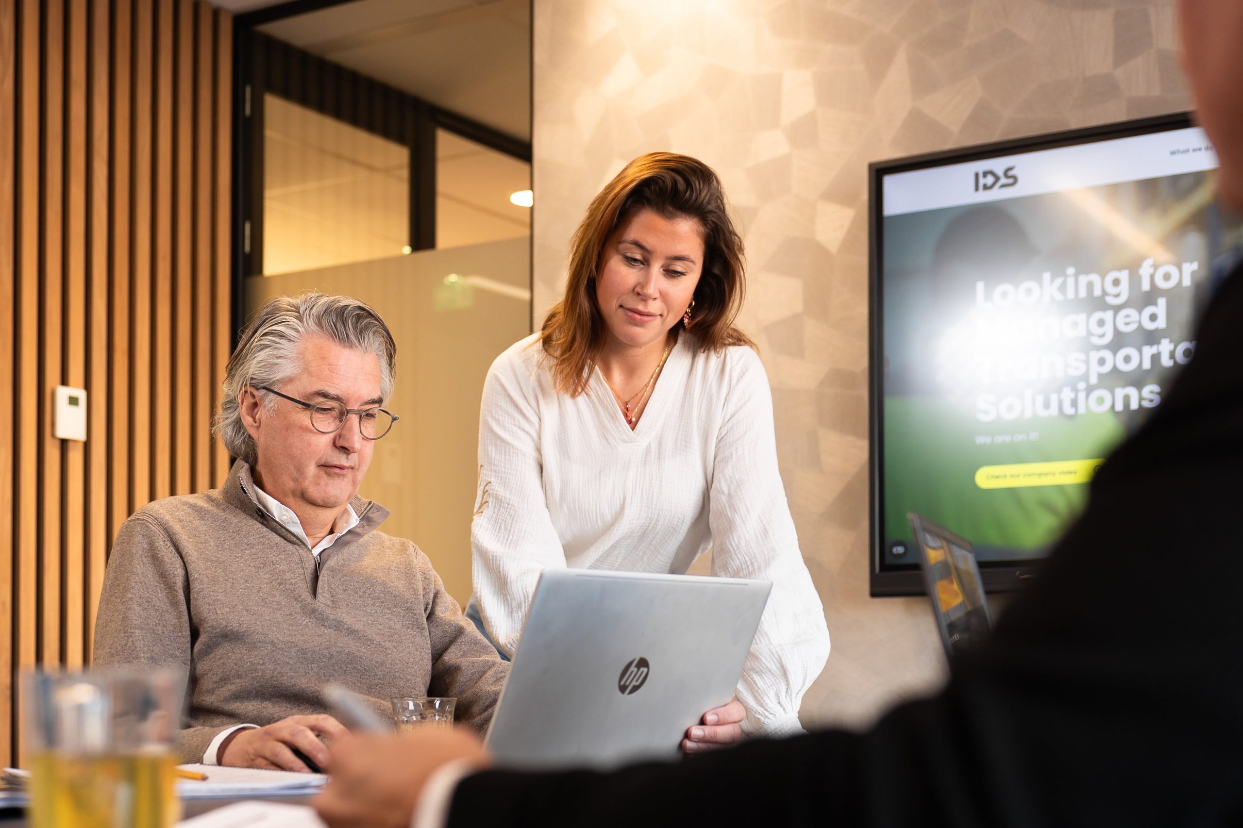Two people are looking at a computer screen and smiling. Behind them you can see the website of IDS and its homescreen